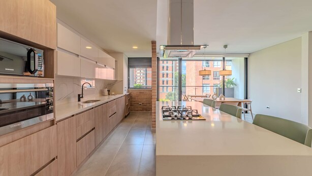 A modern kitchen with wooden cabinets, a built-in oven, and a large island with seating. - w Charming 3BR w Amazing Deco in Medellin (Medellín)