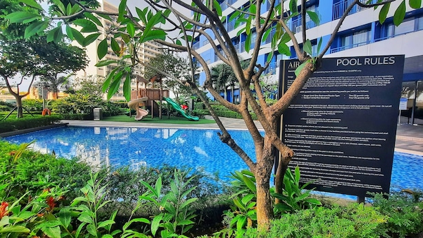 Un espace piscine agrémenté d’un panneau indiquant les règles à respecter, entouré d’une végétation luxuriante et d’une aire de jeux.