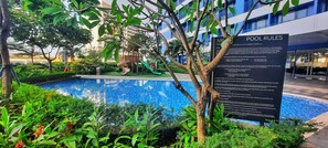 A pool area with a sign detailing pool rules, surrounded by lush greenery and a playground. - Air Residences-Modern studio w/ City skyline view (Makati)
