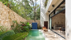 A modern outdoor pool area with stone walls, lush greenery, and a seating area with a sofa and table.