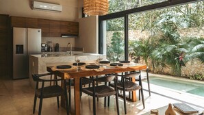A modern kitchen with a large island, a dining area with a wooden table and chairs, and a view of a pool and greenery.