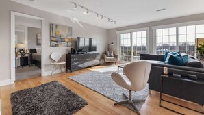A modern living room with a sofa, a TV, and a large window offering a city view. - Penthouse Style Condo with City View (Cincinnati)