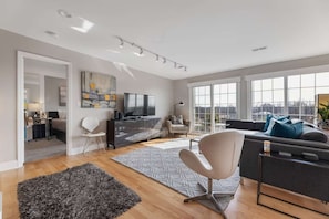 A modern living room with a sofa, a TV, and a large window offering a city view. - Penthouse Style Condo with City View (Cincinnati)
