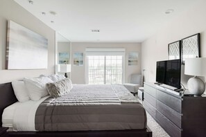 A modern hotel room with a large bed, a flat-screen TV, a dresser, and artwork on the walls. - Penthouse Style Condo with City View (Cincinnati)