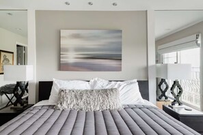 A modern hotel room with a large bed, a view of the sea, and a framed artwork on the wall.