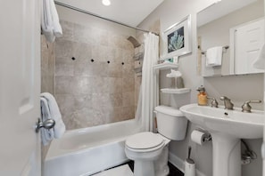 A bathroom with a bathtub, toilet, and sink, featuring beige tiles and white fixtures. - Penthouse Style Condo with City View (Cincinnati)