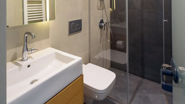 Ein modernes Badezimmer mit einer in Glas eingefassten Dusche, einem weißen Waschbecken und einem großen Spiegel.