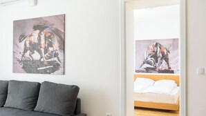 A modern room with a grey sofa, a bed with white linens, and two abstract paintings on the walls. - Tim 3 (Belgrade)