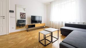 A modern living room with a sofa, a TV, a coffee table, and a herringbone wooden floor. - Tim 3 (Belgrade)