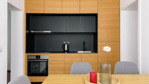 A modern kitchen with wooden cabinets, a black countertop, a stainless steel range hood, and a built-in oven. - Tim 3 (Belgrade)