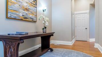 A hallway with a dark wooden console table, a white orchid in a vase, a large abstract painting, and a white door at the end.