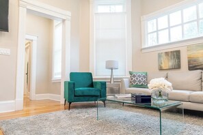 Un salon avec un fauteuil vert, une table basse en verre et un canapé beige.