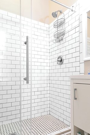 A shower with a glass door, white tiled walls, and a metal shower head.