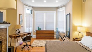 Un dormitorio con cama, escritorio, silla, cómoda y chimenea.