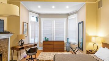 A bedroom with a bed, desk, chair, dresser, and a fireplace.