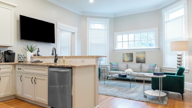 Una cocina moderna con lavavajillas, un televisor de pantalla plana y una zona de comedor con una silla verde y una mesa redonda.