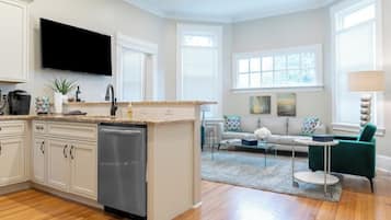 A modern kitchen with a dishwasher, a flat-screen TV, and a dining area with a green chair and a round table.