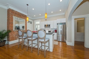 A kitchen with a brick accent wall, white cabinets, stainless steel appliances, and a central island with bar stools.