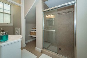 Une salle de bain avec une douche à parois de verre, un lavabo blanc avec un distributeur de savon bleu et une fenêtre au-dessus du lavabo.