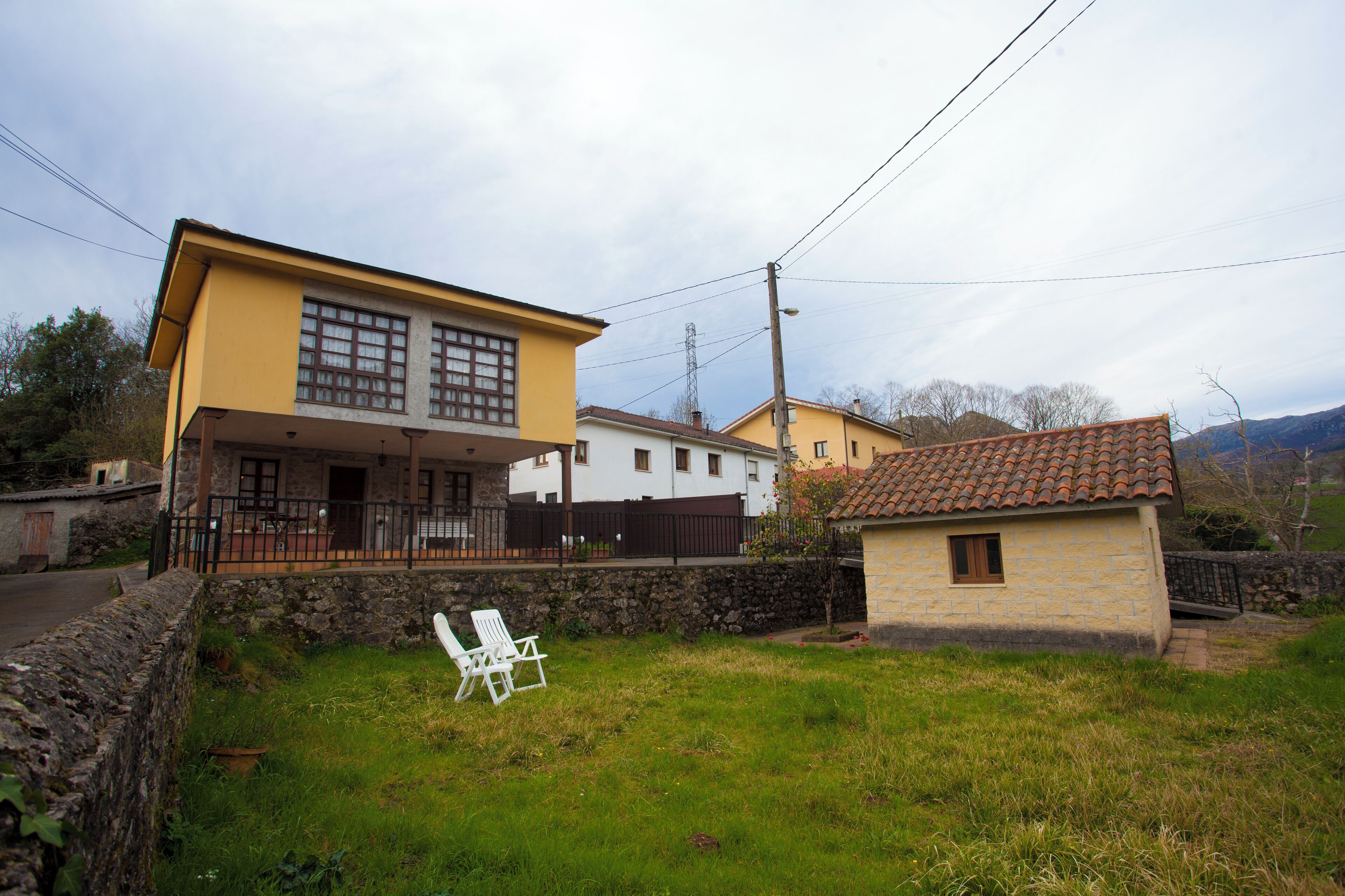 Une maison à deux étages avec un balcon, un petit jardin et une chaise blanche.