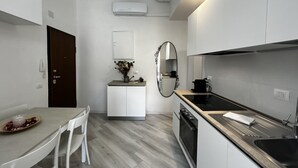 A modern kitchen with white cabinetry, a dining table with chairs, a small island with a vase, and a large mirror. - DEL RE FLORENCE HOME (Firenze)