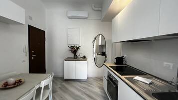 Une cuisine moderne avec des meubles blancs, une table à manger avec des chaises, un petit îlot central agrémenté d'un vase et un grand miroir.