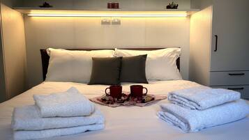 Un lit bien fait, avec du linge de lit blanc, un plateau avec des tasses rouges et des serviettes pliées.