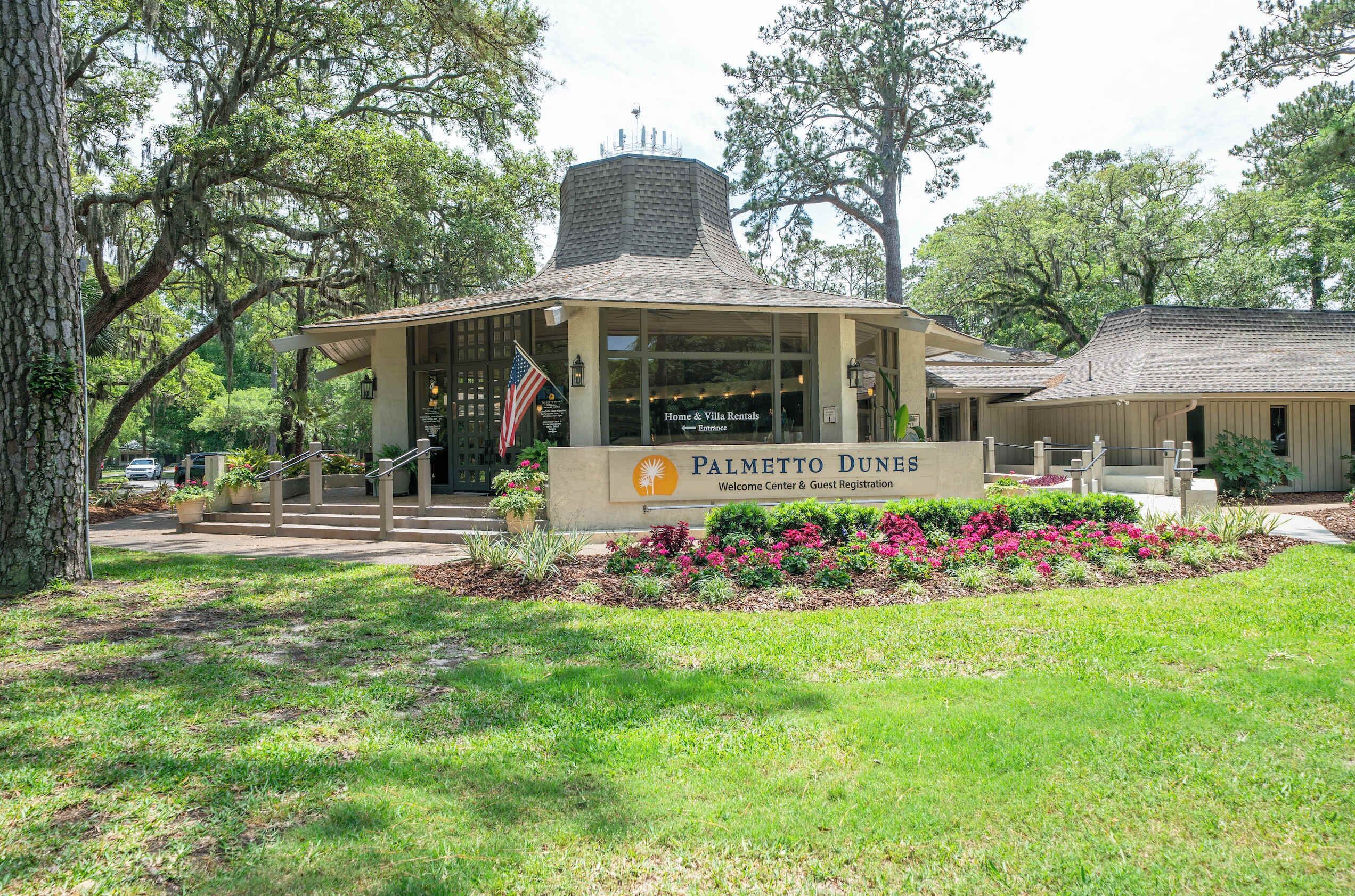 A building with a sign reading "Palmetto Dunes Welcome Center & Guest Registration" with a flag and a small entrance.
