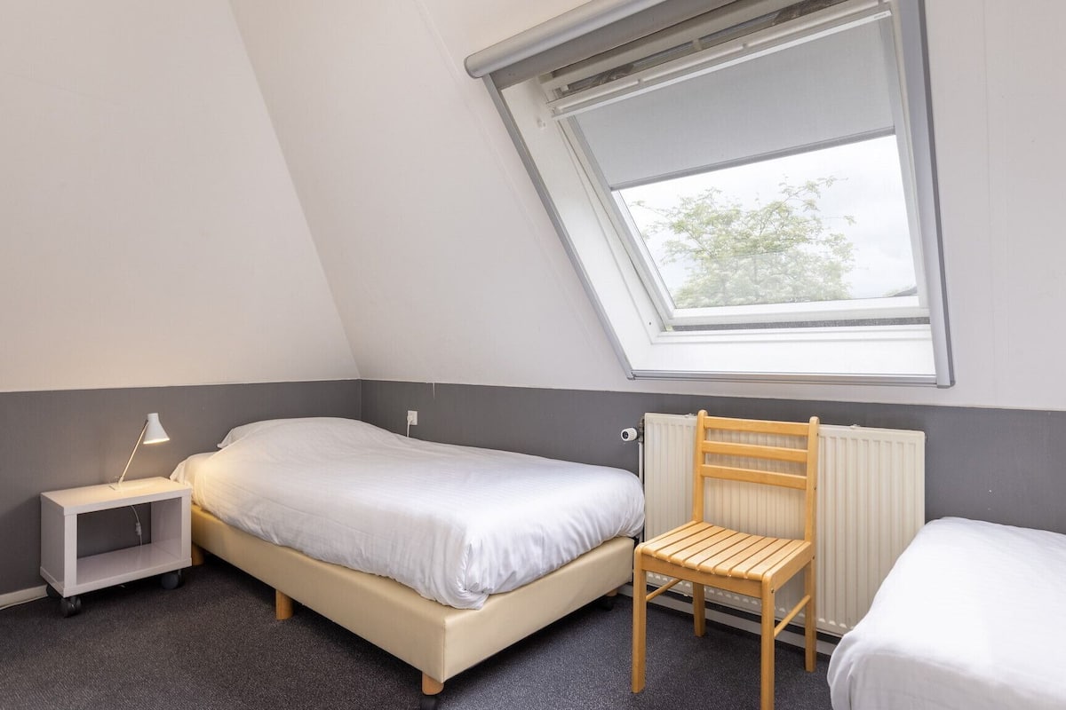 Et lille, godt oplyst værelse med en enkelt seng, en stol, et natbord og en radiator.