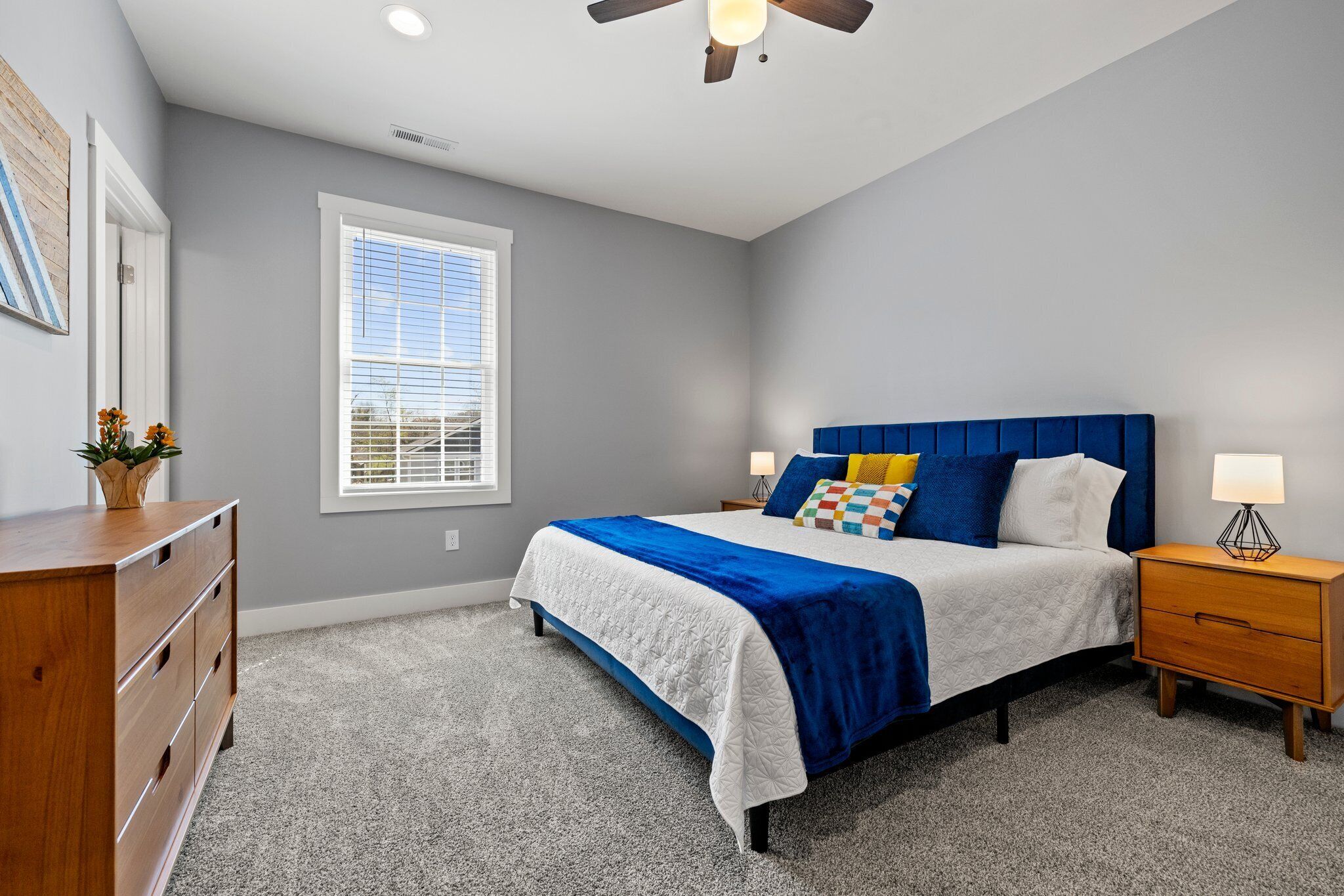 A bedroom with a bed, bedside tables, a dresser, a ceiling fan, and a window.