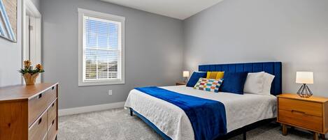 A bedroom with a bed, bedside tables, a dresser, a ceiling fan, and a window.