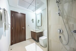 A modern bathroom with a wooden door, a glass shower enclosure, a white sink, and a toilet. - Bloomfields Premium 1BR Reflection (Abu Dhabi)