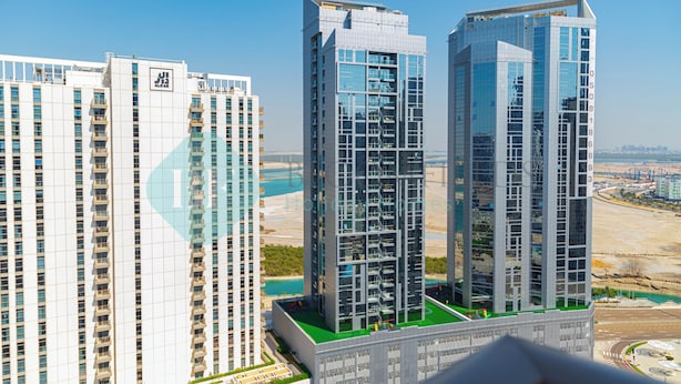 A high-rise building with multiple floors and balconies, surrounded by other tall buildings and a body of water in the background. - Bloomfields Premium 1BR Reflection (Abu Dhabi)