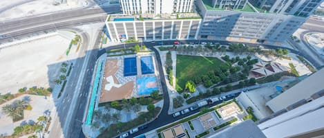 A high-rise building with multiple floors, a swimming pool, and a landscaped area with trees.