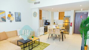 A modern living room with a sofa, coffee table, and artwork on the wall. Adjacent is a kitchen with a refrigerator, microwave, and dining area. - Bloomfields Premium 1BR Reflection (Abu Dhabi)