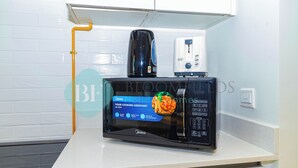 A kitchen with a microwave, a coffee maker, and a toaster on a white countertop. - Bloomfields Premium 1BR Reflection (Abu Dhabi)