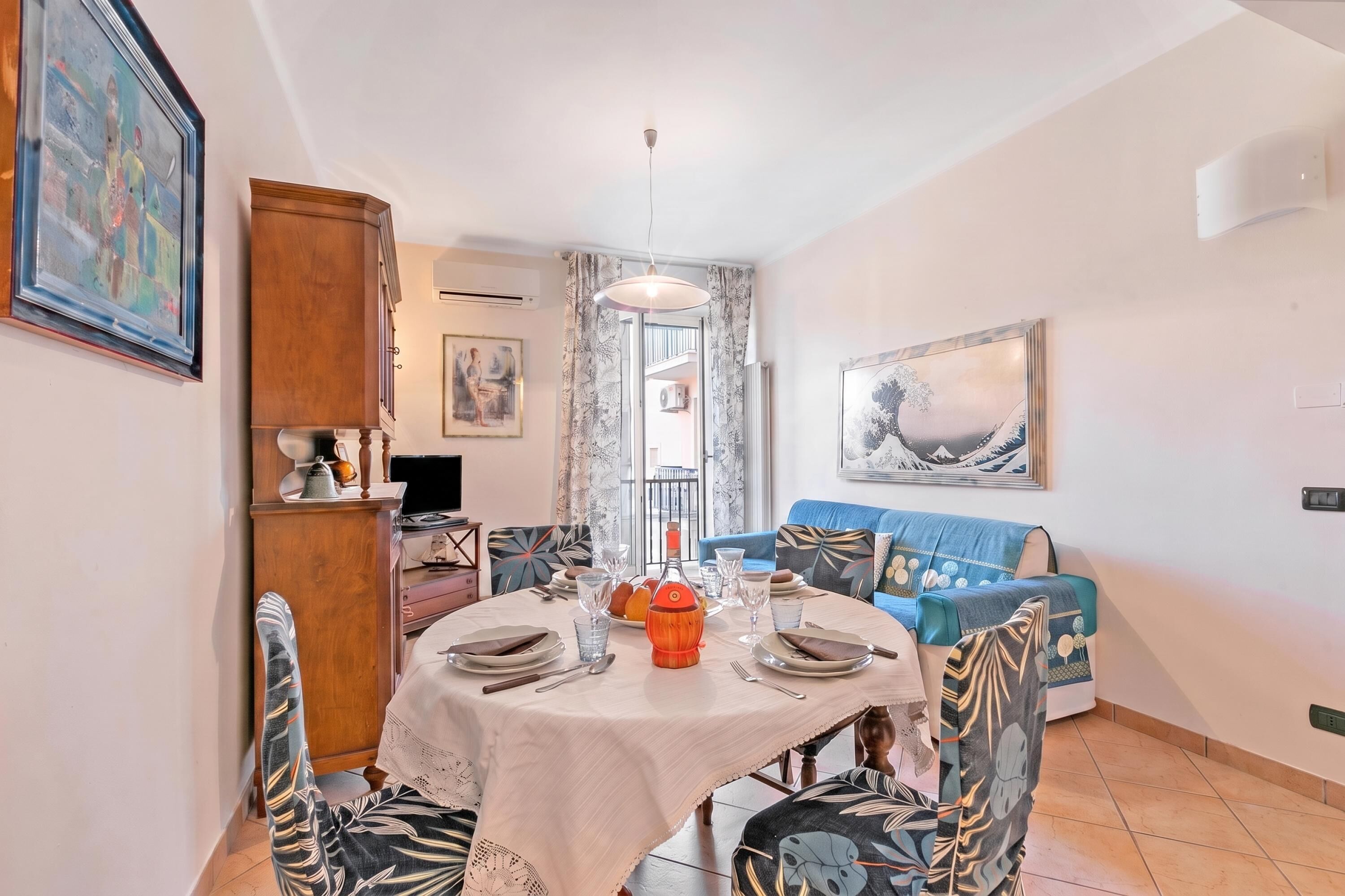 A dining area with a round table set for four, a blue sofa, and a wooden cabinet.