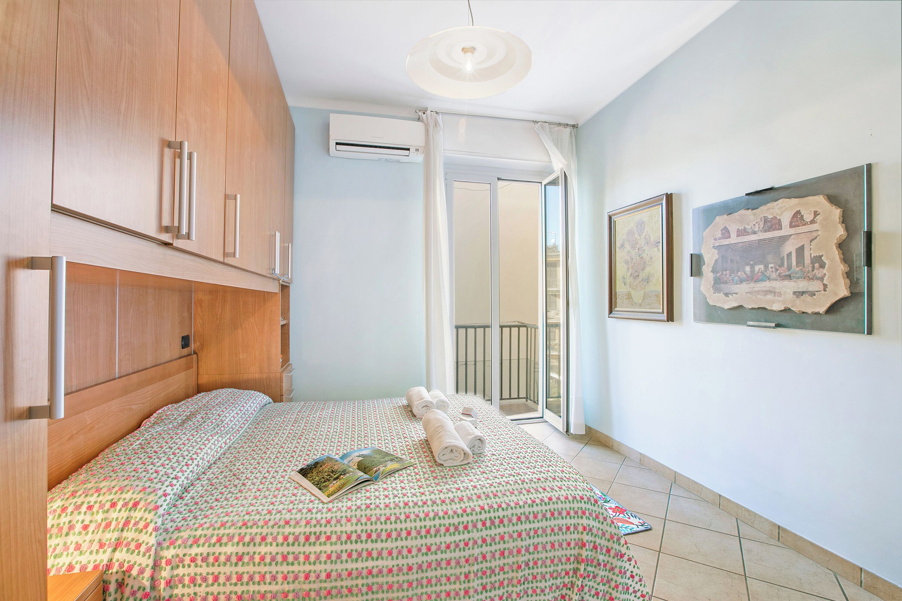 Un dormitorio con cama, mesita de noche, ventana con cortinas y aire acondicionado instalado en la pared.