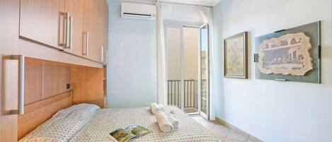 Un dormitorio con cama, mesita de noche, ventana con cortinas y aire acondicionado instalado en la pared.