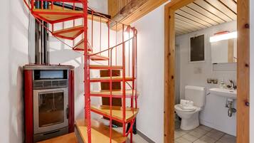 Cocina compacta con horno integrado, una escalera espiral roja y un baño pequeño con inodoro y lavamanos.