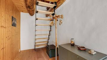 Una habitación con piso de madera, una cama entrepiso con escalera de madera, una pequeña mesa con bandeja y un armario verde.