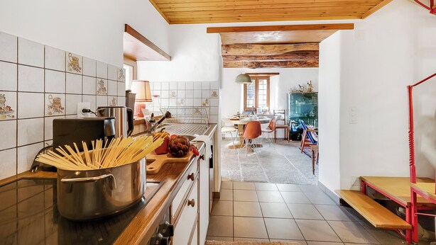 A kitchen with a wooden ceiling, tiled backsplash, and a dining area with a table and chairs. - Rustico Over The Bridge Verzasca (Sonogno)