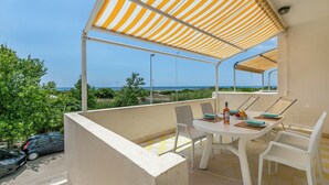 Un balcón con una mesa y sillas blancas, un dosel a rayas y vistas al mar.