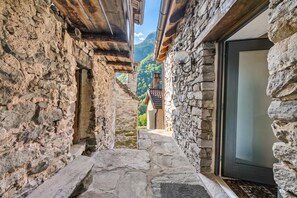 Un estrecho pasillo de piedra con techo de madera y una puerta que da a una habitación con vistas a montañas.