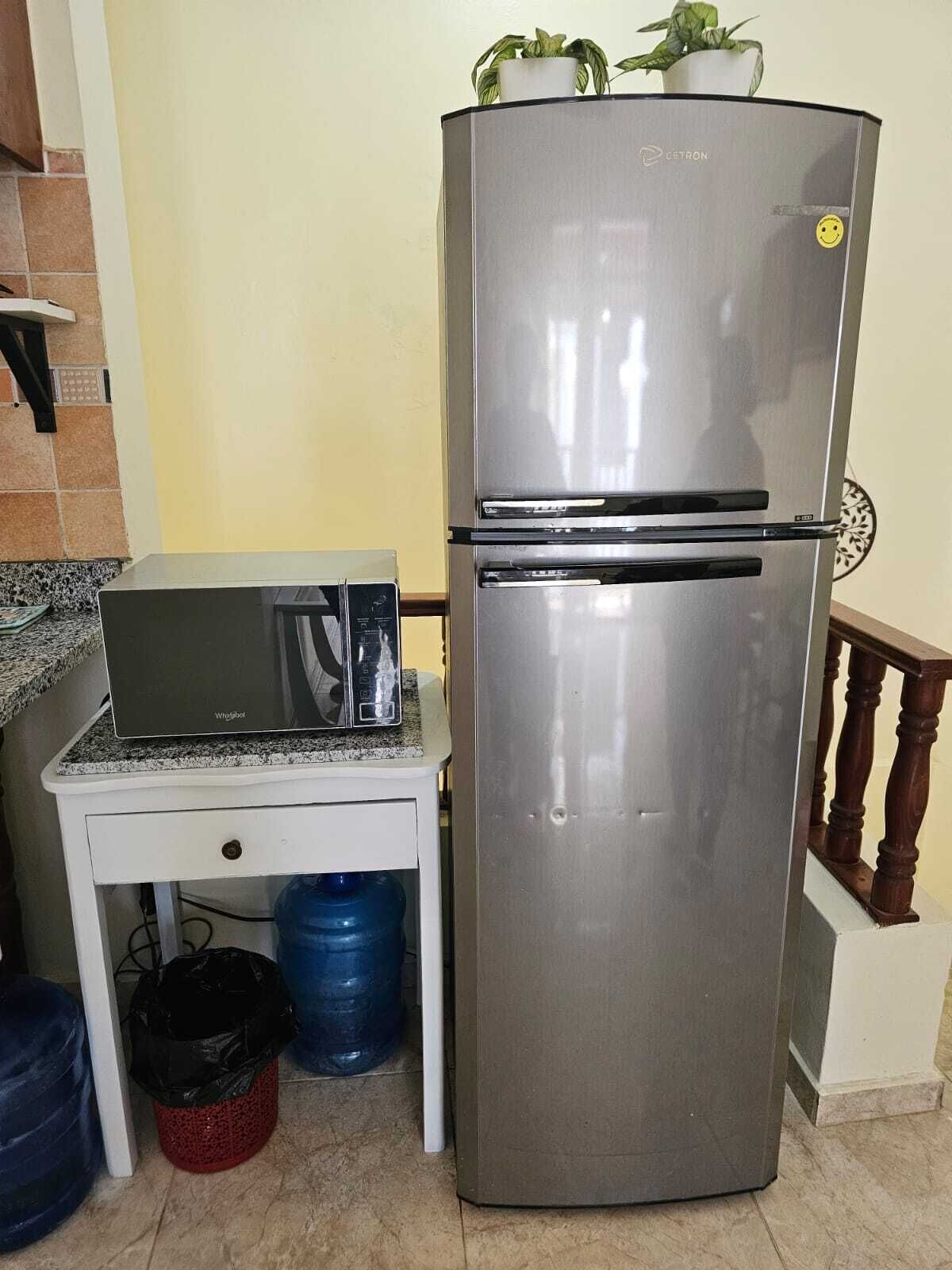 Een kleine keuken met een roestvrijstalen koelkast, een magnetron op een klein aanrecht en een waterdispenser.