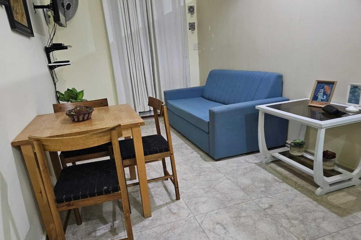 Ein kleiner Wohnbereich mit einem Holztisch und Stühlen, einem blauen Sofa und einem weißen Nachttisch mit Bilderrahmen.