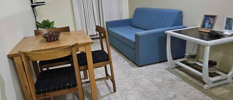 A small living area with a wooden table and chairs, a blue sofa, and a white side table with a picture frame.