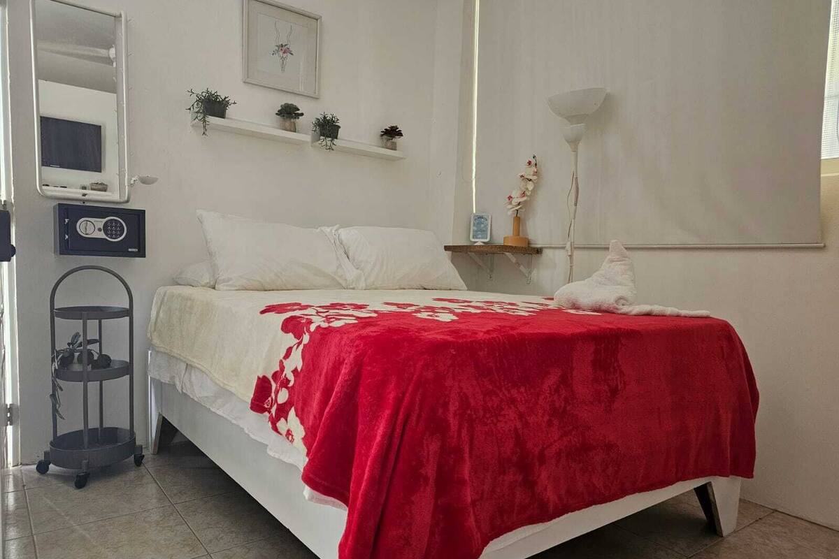 Ein Schlafzimmer mit einem Bett, einem Nachttisch, einem Wandregal mit Pflanzen, einer Nachttischlampe und einem kleinen Tisch mit einer Pflanze.