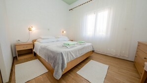A bedroom with a bed, bedside tables, a nightstand, a window with curtains, and a wooden floor. - Apartmani Mijatović (Lopar)