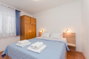 A bedroom with a bed, two bedside lamps, a wardrobe, and a window with curtains. - Apartmani Mijatović (Lopar)